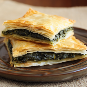 Crispy golden phyllo dough dishes, including spanakopita, baklava, and phyllo-wrapped asparagus, arranged on a wooden table with fresh ingredients like butter, honey, and nuts.